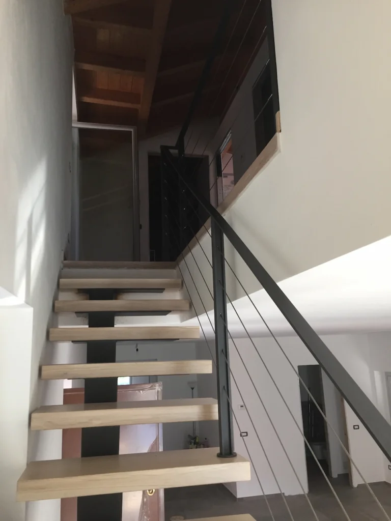 Scala moderna sospesa per arredamento d'interno con gradini in legno chiaro e struttura portante in metallo grigio.